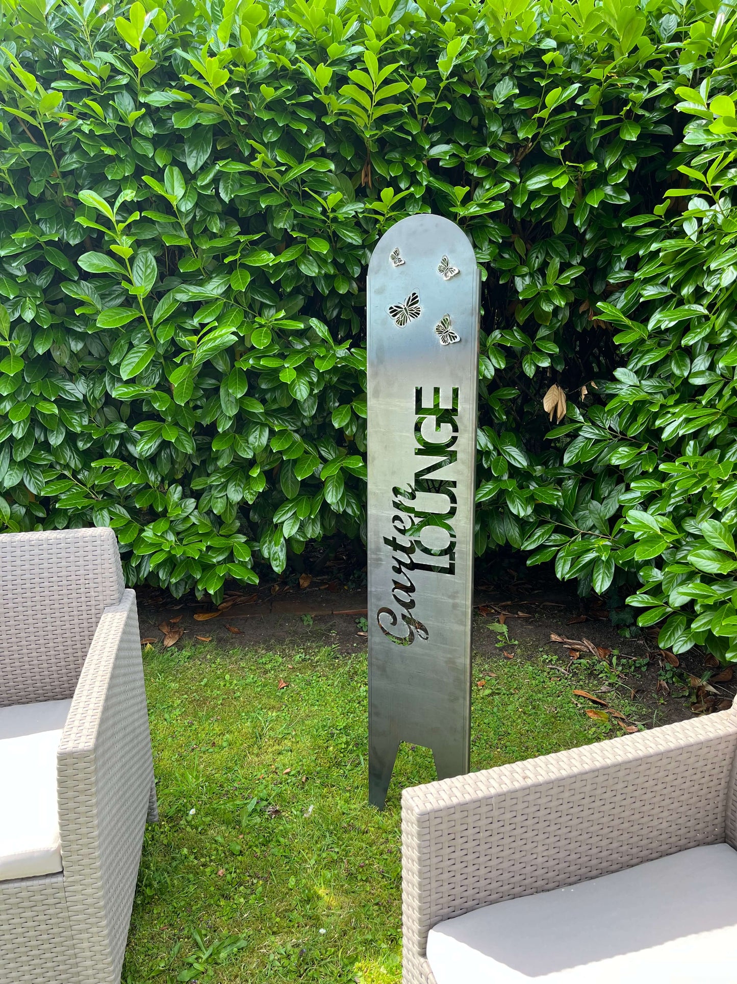 Gartenstecker in Silber vor einer grünen Hecke stehend mit Loungemöbeln.