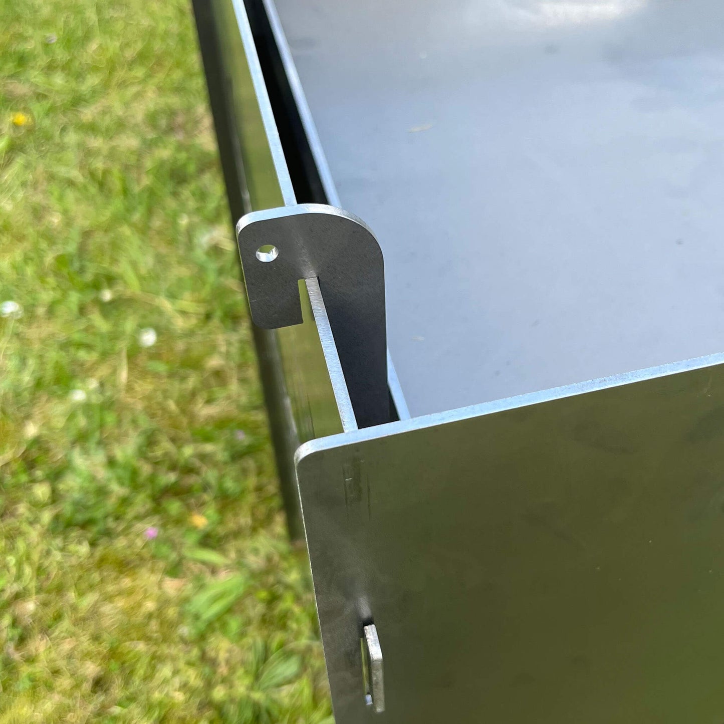 Die Ecke einer Feuertonne. Eingerasteter Hacken für die Aschewanne.