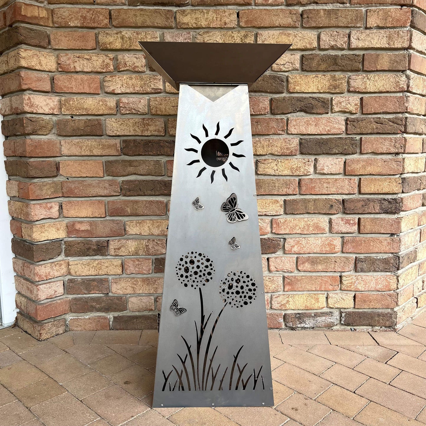 Rechteckige Blumensäule mit Pflanzenschale vor einer Steinwand. Mit Blumen, Schmetterlingen und einer Sonne.