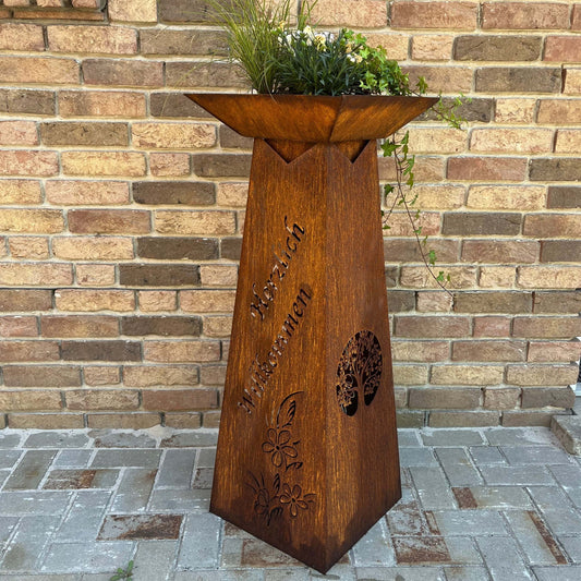 bepflanzte Blumensäule mit Patina vor Hauswand