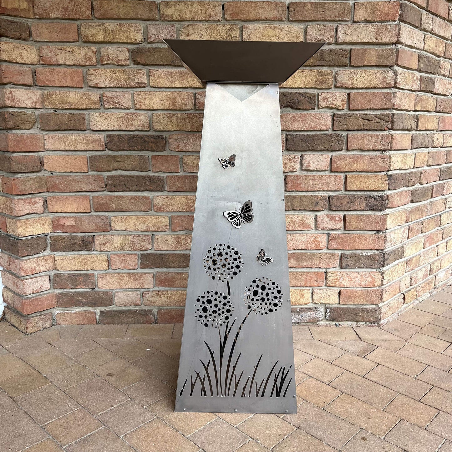 Graues Rechteck mit Pusteblumen und Schmetterlingen vor einer Hauswand