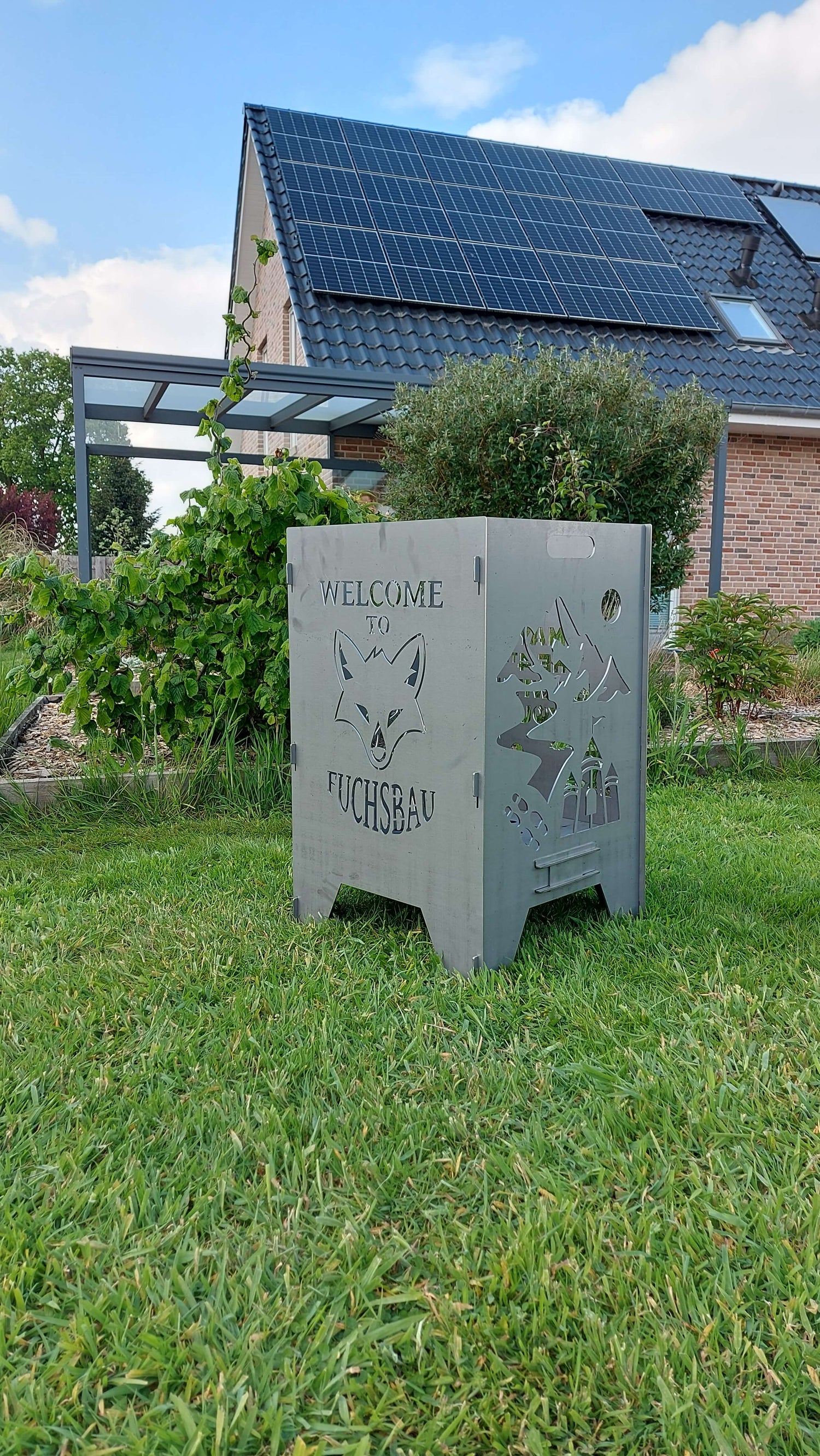 Viereckige Feuertonne in einem Garten mit einem Haus im Hintergrund