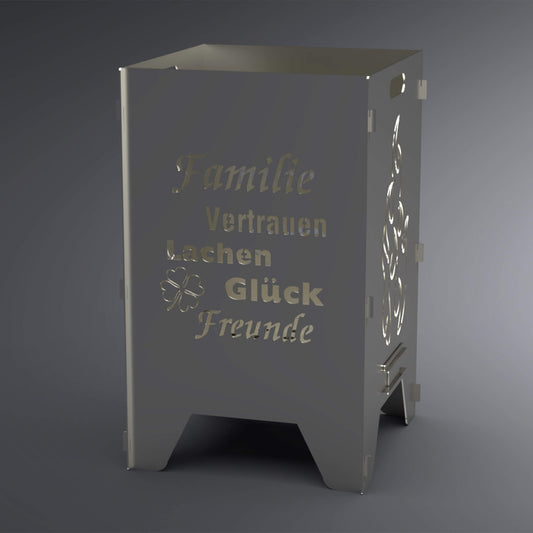 Feuertonne mit dem Spruch: "Familie, Vertrauen, Lachen, Glück, Freunde" und einem Kleeblatt auf zwei Seiten. Auf zwei Seiten ist ein Flammen-Motiv. Die Seite mit dem Spruch steht im Vordergrund.
