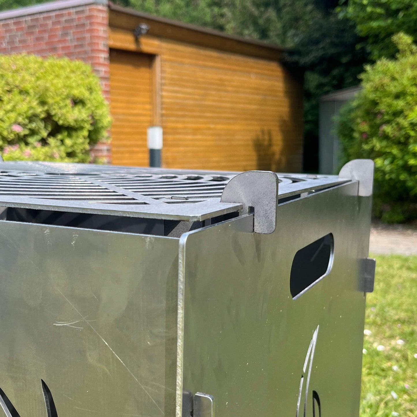 Ecke einer Feuertonne. Eingerastetes Grillrost auf der Feuertonne.