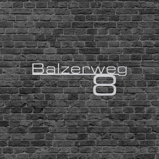 Eine Wanddekoration die die Adresse wiedergibt. Straßenname steht auf einer schmalen Linie und da drunter steht die Hausnummer. Schild hängt an einer Hauswand.