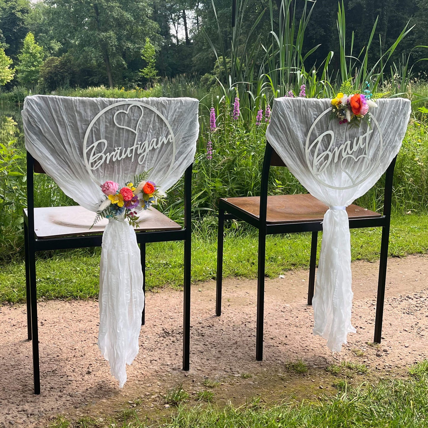 zwei Stühle vor einem See, Stühle sind von hinten mit hochzeitskränzen bunt dekoriert