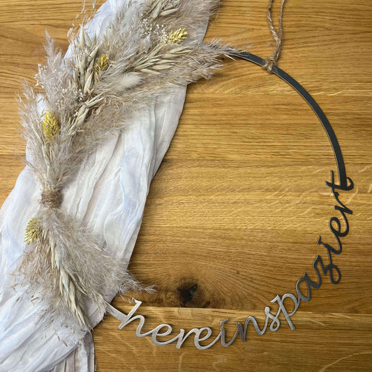 Dekorierter runder Türkranz mit Trockenblumen auf einem weißem Musselintuch auf einem Holz Hintergrund.