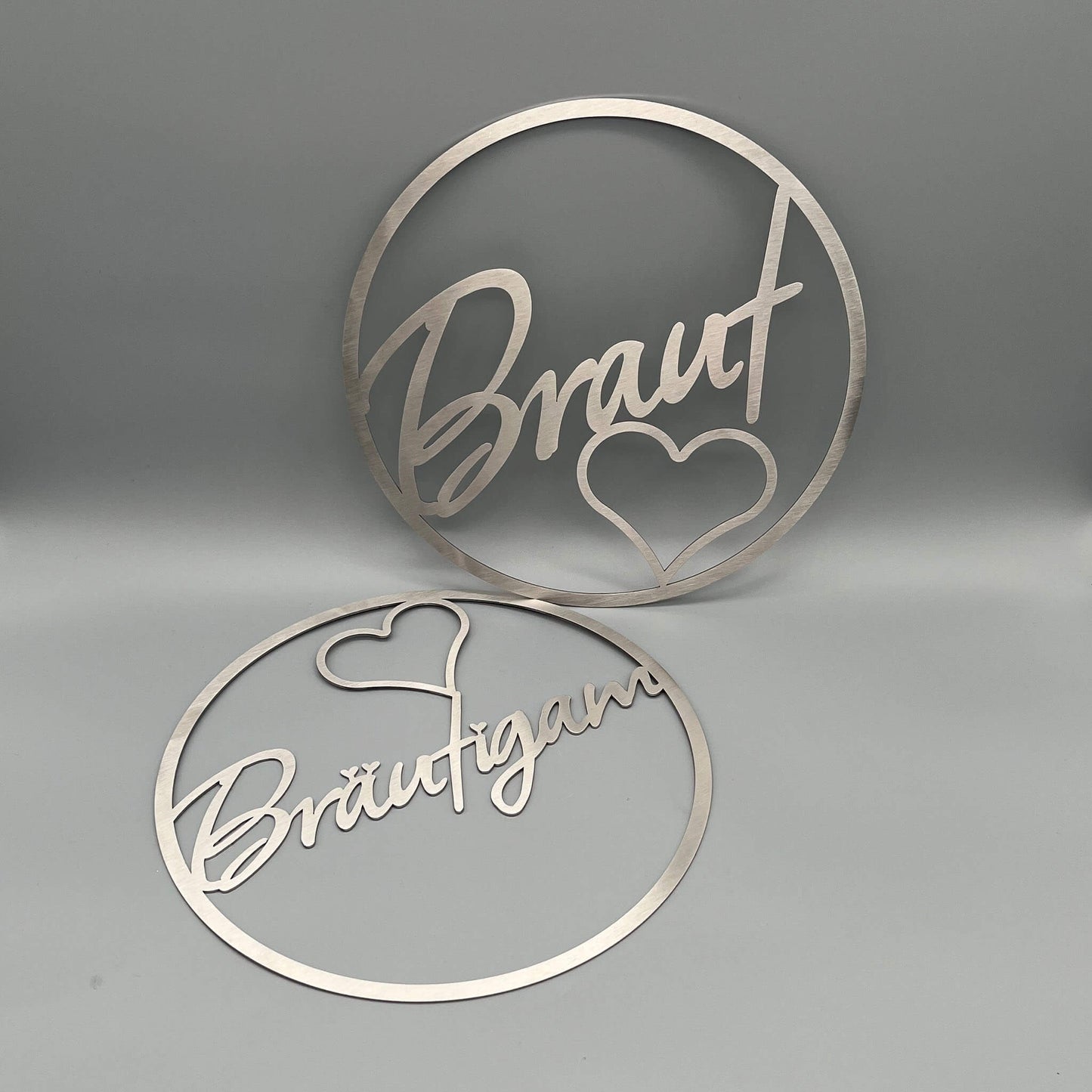 Zwei Dekoringe, stehender Ring mit Innenschrift Braut und einem Herz darunter, liegender Kranz mit der Innenschrift Bräutigam und einem Herz über t.