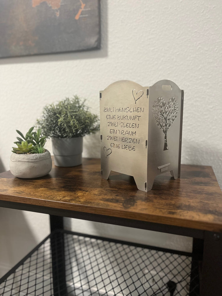 Teelichthalter in Silber auf einer Holzoberfläche. Links daneben sind kleine Pflanzen.