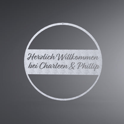 Dünner, ausgehöhlter Kreis. In der Mitte ist ein Balken. Dort steht: "Herzlich Willkommen bei Name & Name".