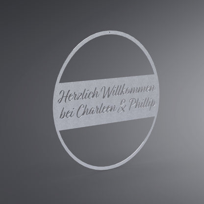 Dünner, ausgehöhlter Kreis. In der Mitte ist ein Balken. Dort steht: "Herzlich Willkommen bei Name & Name". Seitliche Ansicht.
