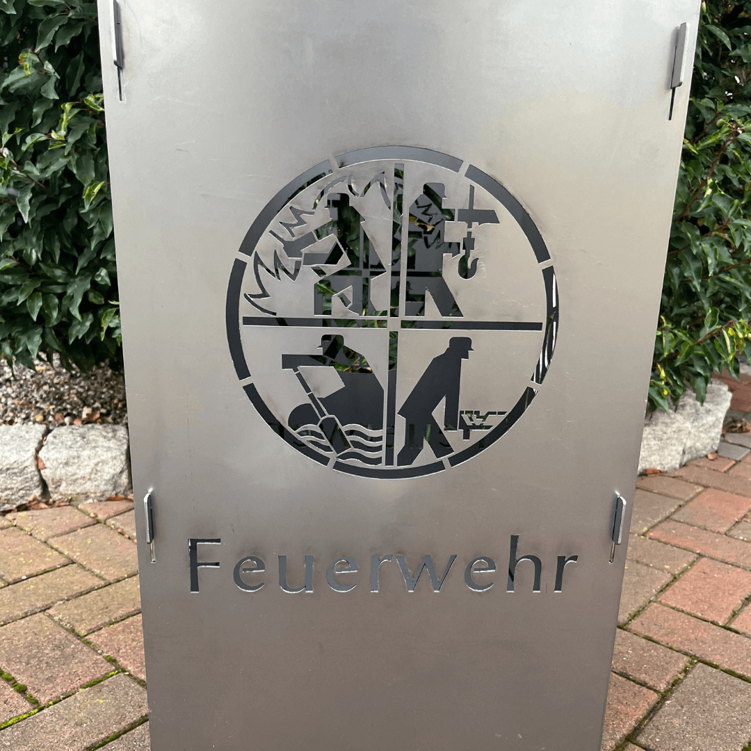 Aus gelasertes Feuerwehrwappen in einer Metall Feuertonne. Schriftzug Feuerwehr unter dem Wappen auf der Feuertonne. 