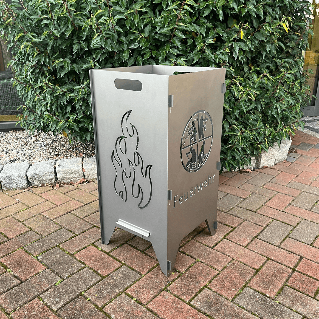 Feuertonne mit einem runden Feuerwehrwappen in der Mitte und darunter steht: "Feuerwehr" auf zwei Seiten. In dem runden Wappen sind Strichmännchen die verschiedenen Tätigkeiten nachgehen. Auf den anderen beiden Seiten befindet sich das Flammen-Motiv.