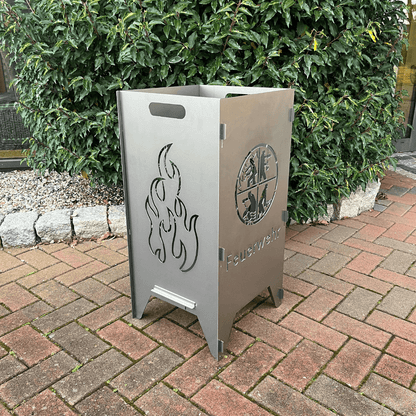 Feuertonne mit einem runden Feuerwehrwappen in der Mitte und darunter steht: "Feuerwehr" auf zwei Seiten. In dem runden Wappen sind Strichmännchen die verschiedenen Tätigkeiten nachgehen. Auf den anderen beiden Seiten befindet sich das Flammen-Motiv.