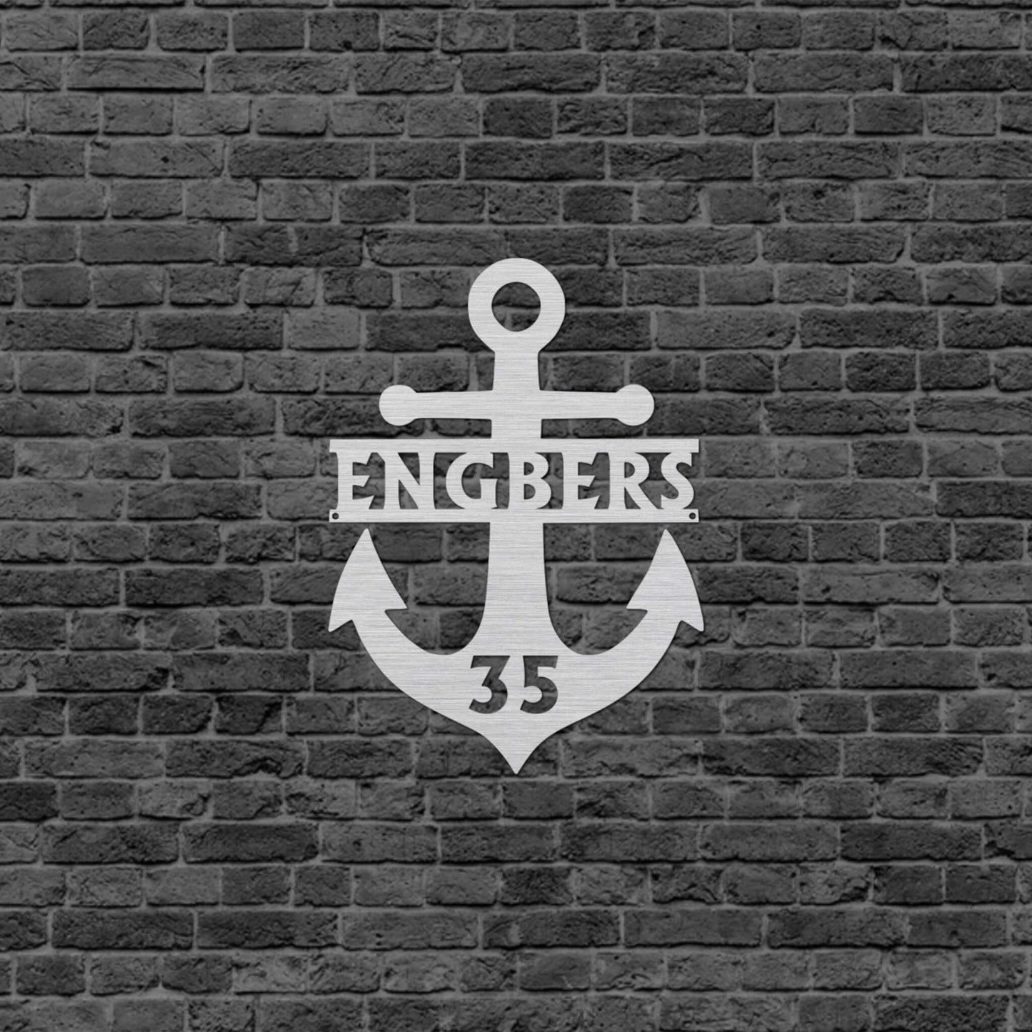Eine Wanddekoration in Form eines Ankers mit dem Familiennamen in der Mitte und unten ist eine Zahl eingraviert. Schild hängt an einer Hauswand.