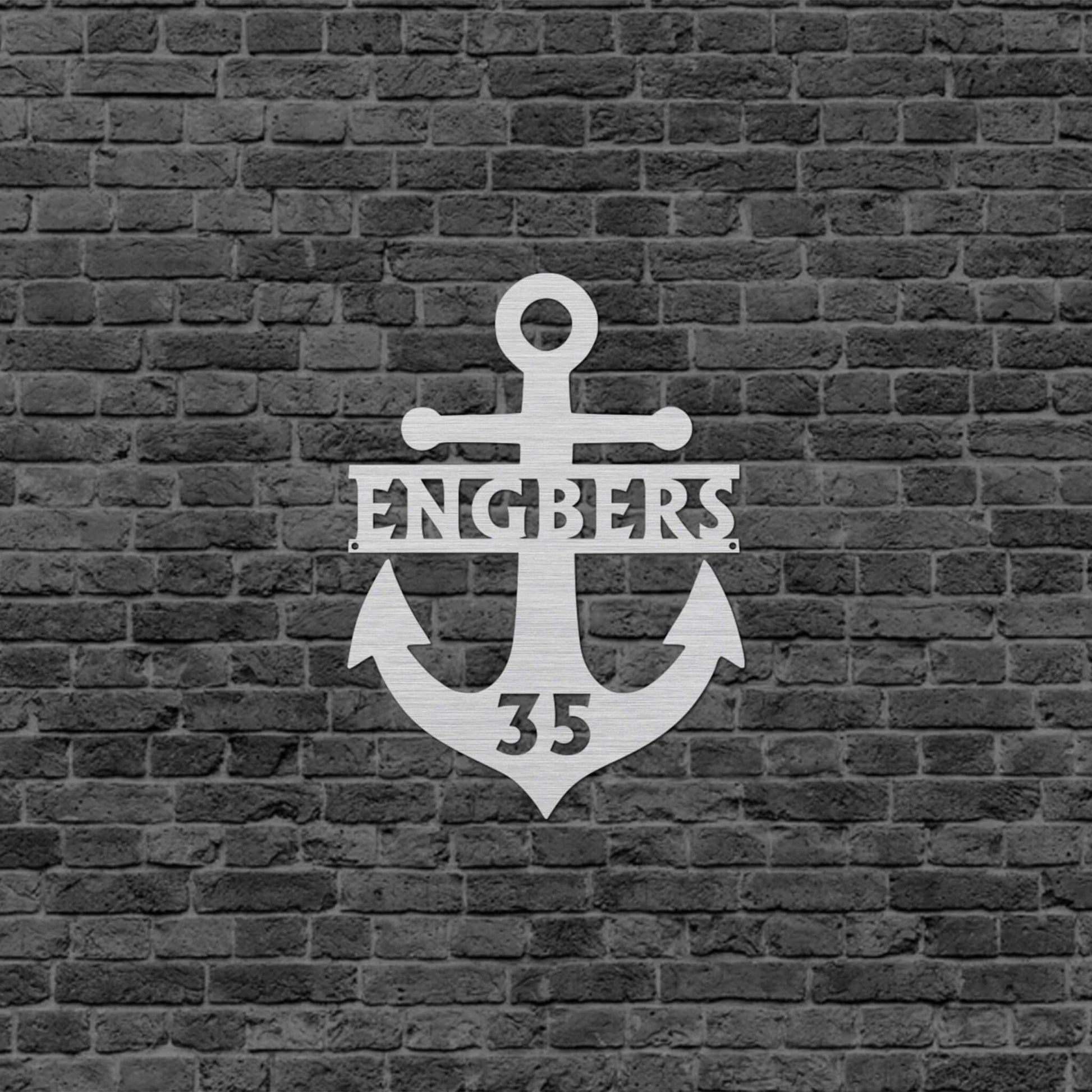 Eine Wanddekoration in Form eines Ankers mit dem Familiennamen in der Mitte und unten ist eine Zahl eingraviert. Schild hängt an einer Hauswand.