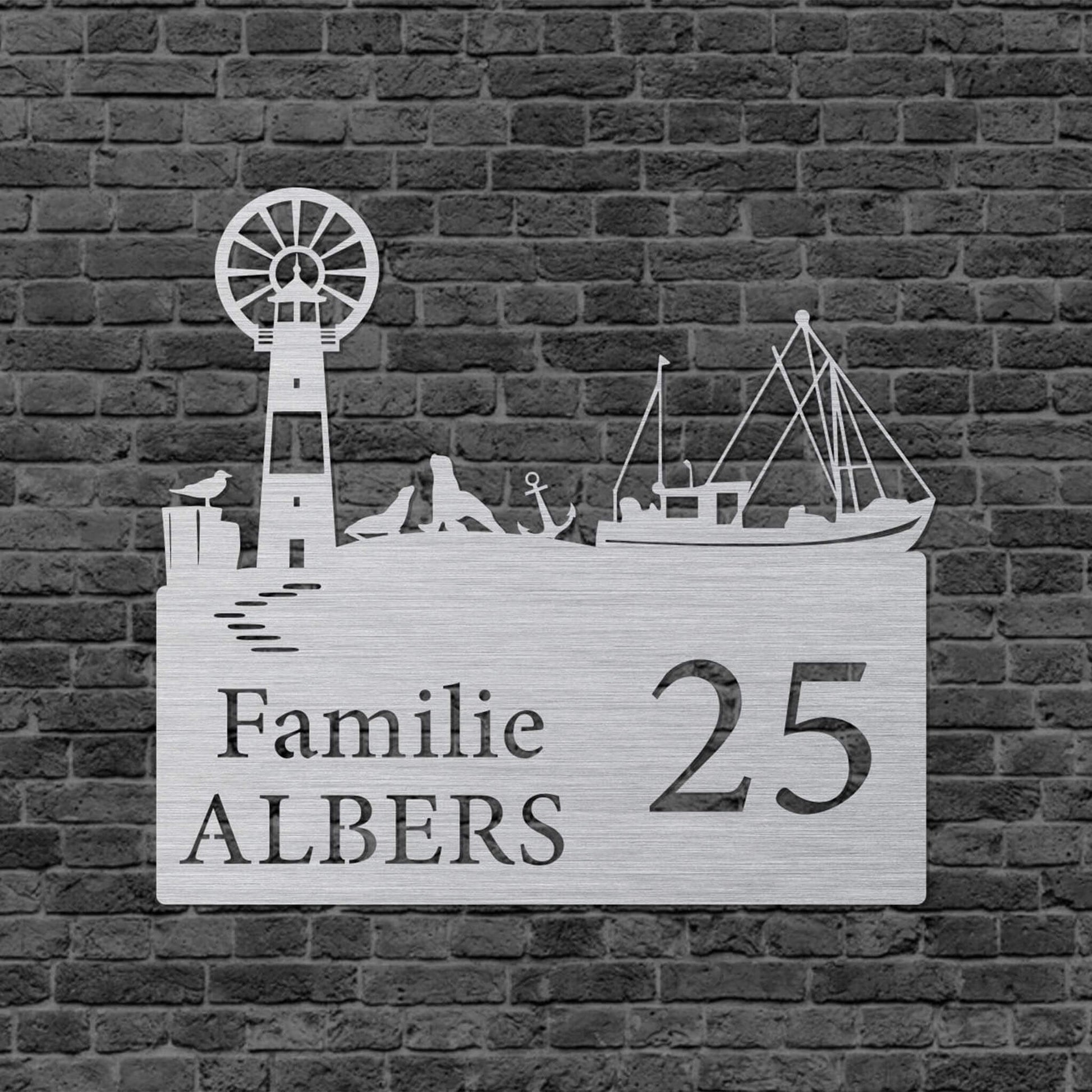 Eine Wanddekoration in Form eines Rechtecks. Rechts steht Familie und darunter der Familienname. Links steht die vergrößerte Hausnummer. Auf der oberen Kante ist eine Leuchtturm, ein Schiff, ein Anker, eine Möwe und Seelöwen abgebildet. Das Schild hängt an einer Hauswand.