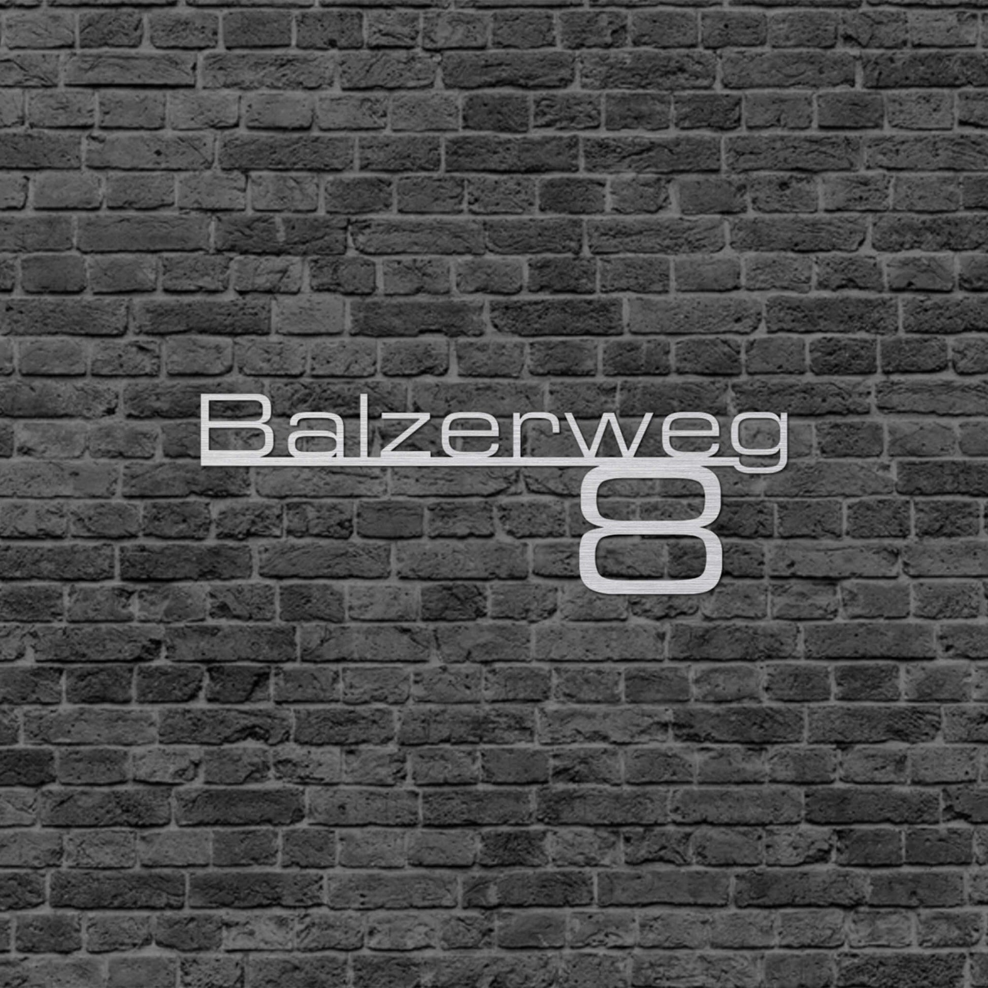 Eine Wanddekoration die die Adresse wiedergibt. Straßenname steht auf einer schmalen Linie und da drunter steht die Hausnummer. Schild hängt an einer Hauswand.