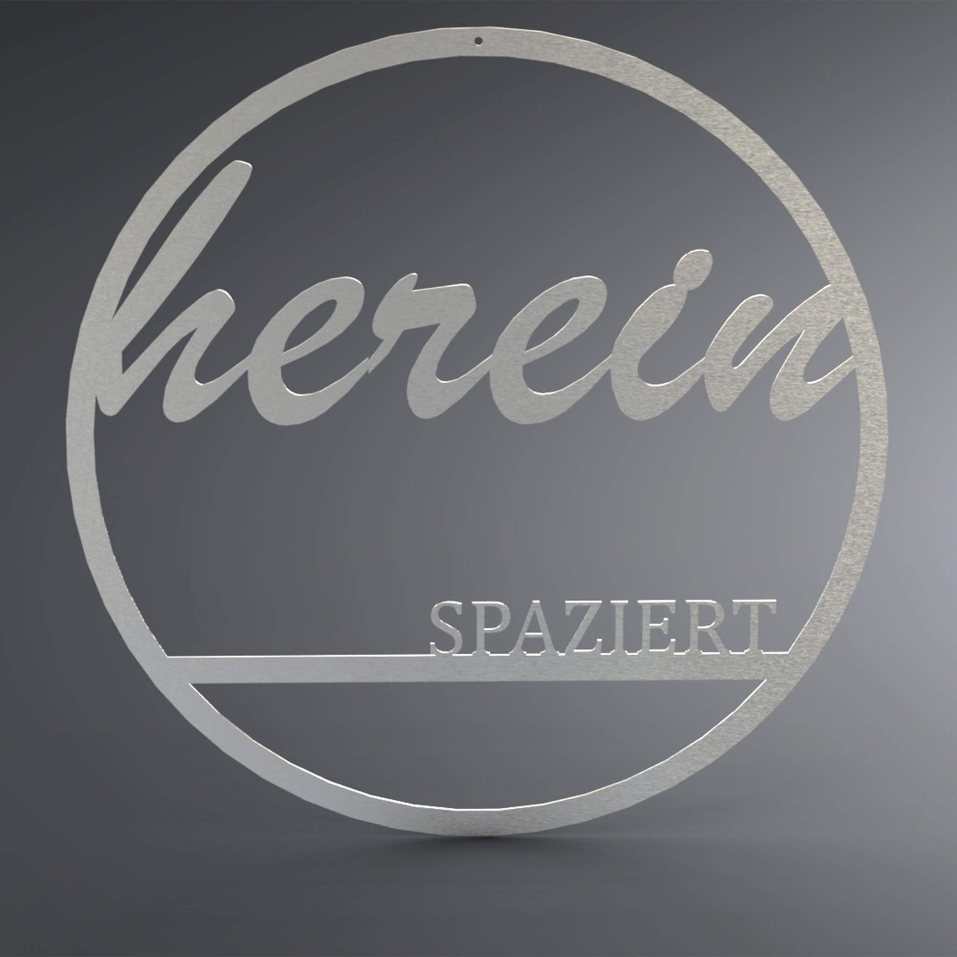 Dünner, ausgehöhlter Kreis. Oben steht verschnörkelt: "herein" und unten steht auf einer Linie in Druckbuchstaben: "spaziert".