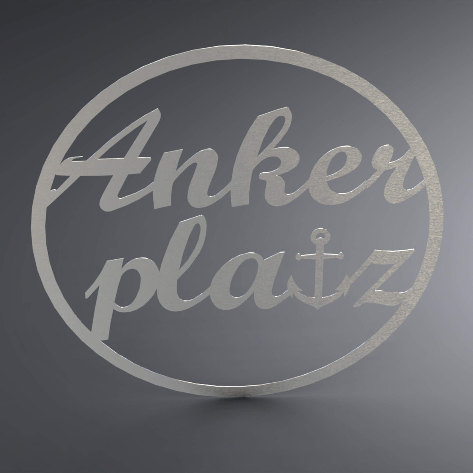Dünner, ausgehöhlter Kreis. Über die komplette Lücke steht: "Ankerplatz" groß und verschnörkelt. Das t wurde gegen einen Anker ersetzt.