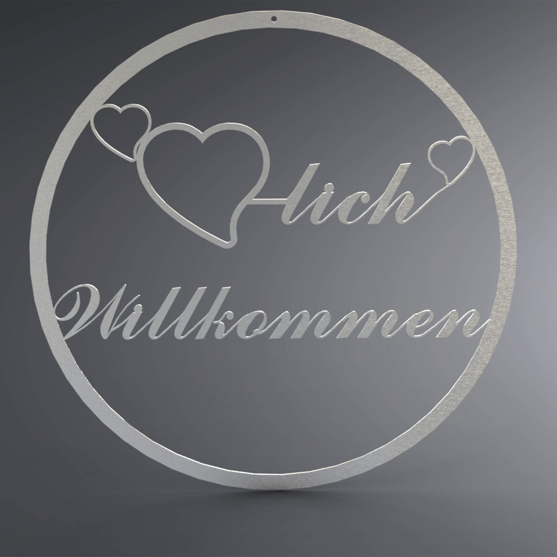 Dünner, ausgehöhlter Kranz. Mittig ist ein ausgehöhltes Herz verbunden mit dem Wort: "-lich". Auf beiden Seiten befindet sich noch ein kleines, ausgehöhltes Herz. Da drunter steht Willkommen verschnörkelt.