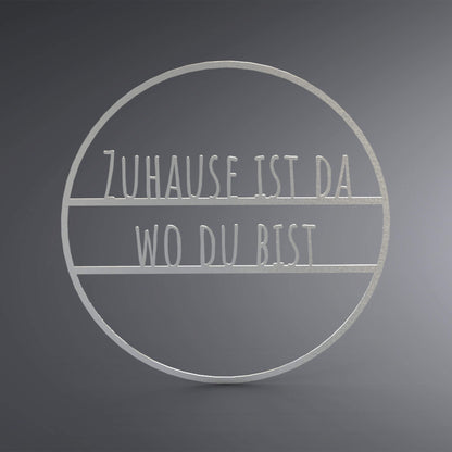 Dünner, ausgehöhlter Kreis. In der Mitte steht: "Zuhause ist da wo du bist".