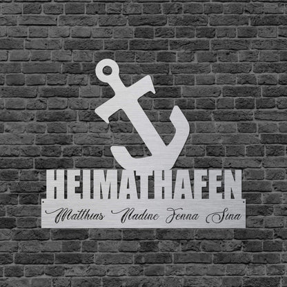 Eine Wanddekoration mit einem Anker, den Spruch Heimathafen und eingravierte, individuelle Namen. Schild hängt an einer Hauswand.