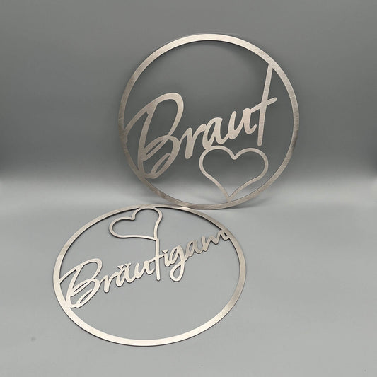 Zwei Dekoringe, stehender Ring mit Innenschrift Braut und einem Herz darunter, liegender Kranz mit der Innenschrift Bräutigam und einem Herz über t.