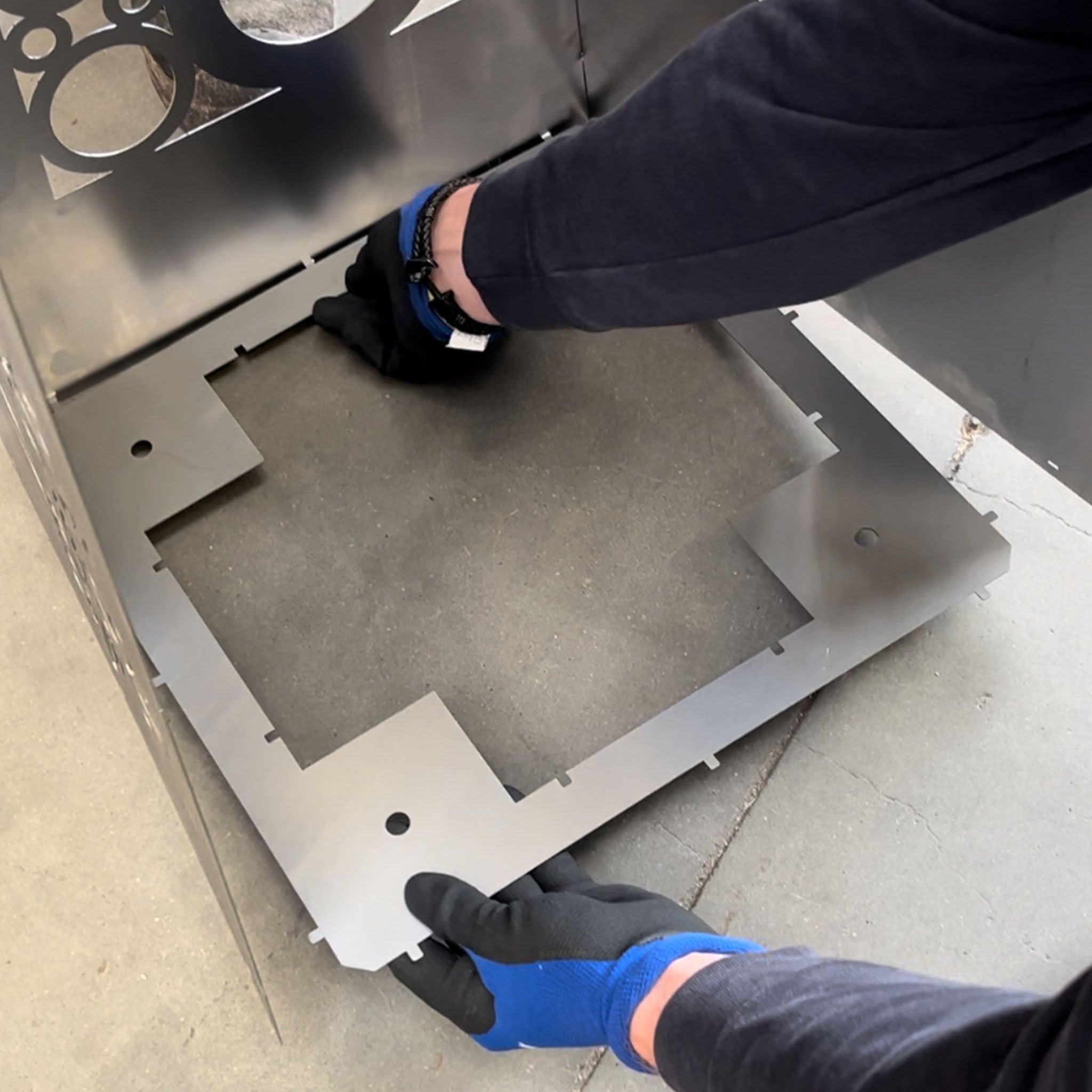 Zwei Hände halten ein viereckiges Bauteil für ein Stahl-Produkt. Das Bauteil wird an das unfertige Produkt gelegt. 